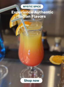 Tropical mixed drinks garnished with orange slices and straws on a bar counter at Mystic Spice Indian Restaurant.